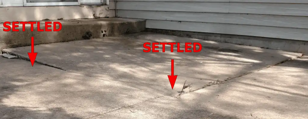 Concrete patio next to a house with two red arrows labeled SETTLED pointing to sunken and cracked areas where the concrete has settled unevenly.