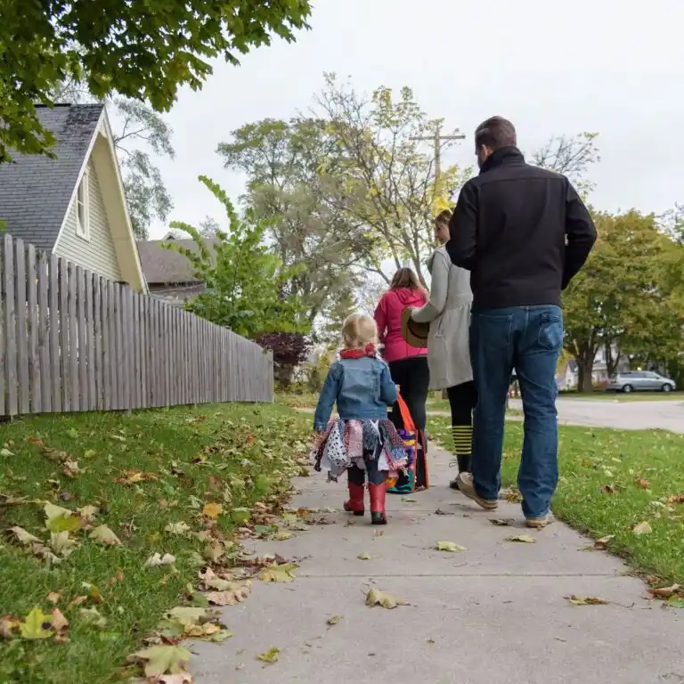 A family of four, including two young children in colorful outfits, walks together on a sidewalk in a residential neighborhood on a cloudy day, perhaps after raising concrete in Inverness to ensure safe and even pathways.