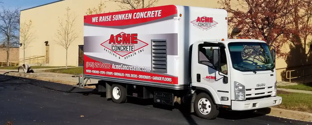 A white Isuzu box truck with Acme Concrete and contact info on the side is parked on a street near a beige building and leafless trees. The truck advertises Raising Concrete in Franklinville, highlighting their expert concrete raising and repair services.