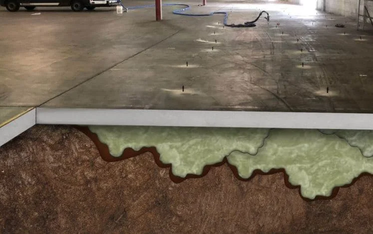 A warehouse floor with a cutaway showing foam injection beneath the concrete slab, illustrating ground stabilization and floor leveling—a technique also used for Garage Floor Lifting in Crystal Lake.